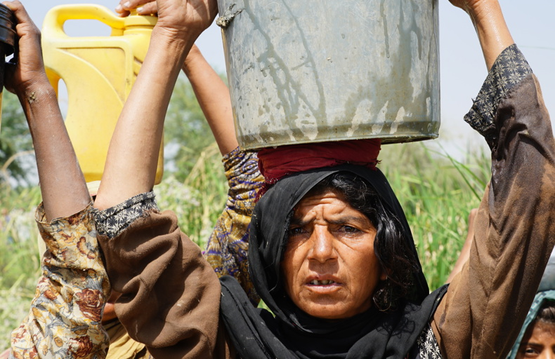 Elderly woman carrying water with others walking beside her
